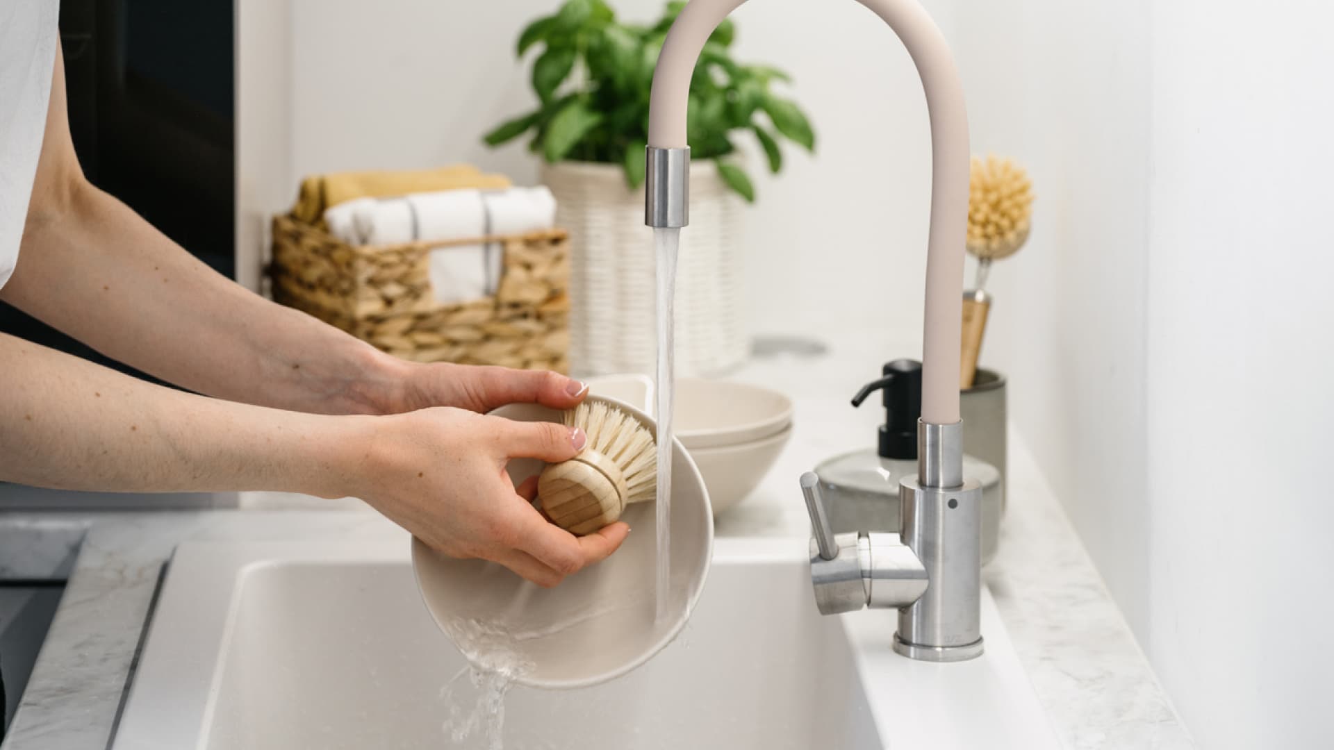 Hands washing dishes at sink.